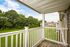 Charming apartment balcony with white railings, offering serene views of lush green trees and open lawns.