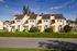 Charming row of townhouses with modern design set against a clear blue sky, lush green lawns, and a serene neighborhood atmosphere.