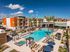 Luxurious apartment complex showcasing a stunning pool surrounded by palm trees, modern architecture, and outdoor lounging areas under clear blue skies.