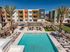 Modern apartment complex with vibrant exterior and stunning pool area, featuring palm trees, stylish lounge chairs, and cozy pergolas for relaxation.
