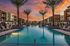 Luxurious apartment complex with a stunning palm-lined pool at sunset, offering resort-style living.