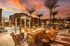 Luxurious outdoor patio with a cozy fire pit surrounded by stylish chairs, overlooking a sparkling pool at sunset.