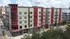 Modern multi-story building with beige and red accents, featuring large windows and vibrant city ambiance.