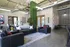 Modern lounge with black leather sofas, vibrant greenery, and industrial ceiling design.