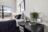 Modern bedroom with cozy bed, decorative pillows, and stylish artwork. Bright natural light from large window, complemented by a sleek desk with plant, clock, and inspirational decor.