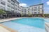 Modern apartment complex with a luxurious swimming pool, surrounded by sun loungers and stylish landscaping, under a bright blue sky.