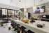Contemporary kitchen space with a sleek island and seating, elegantly set with gourmet mini sliders, pastries, and champagne bottles, enhanced by modern pendant lighting and a backdrop of large windows showcasing a vibrant cityscape.