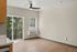 Bright, modern apartment interior with sleek ceiling fan, large windows, and wood flooring, offering a serene greenery view.
