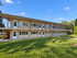 Charming two-story apartment building with modern balconies, surrounded by lush green lawn and clear blue sky.
