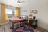 .Private bedroom with natural light Auburn student apartment Bright, modern bedroom with vibrant decor, featuring a large window with yellow curtains, a stylish bed with storage, and a cozy workspace with chic artwork.