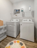 In unit washer and dryer Auburn student apartment. Modern laundry room with a sleek washer and dryer set, stylish shelving and vibrant decor accents on warm wooden flooring.