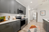 Open concept kitchen and living room Auburn student housing. Modern kitchen with sleek grey cabinets, stainless steel appliances, and stylish decor leads to a convenient laundry area.