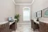 Elegant home office with natural light, featuring wicker chairs, a sleek marble desk, modern computer setup, and lush indoor plants.
