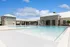 Luxurious apartment complex featuring a sparkling outdoor pool surrounded by elegant stone architecture under a clear blue sky.