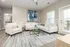 Bright and elegant living room with modern decor, featuring a cozy cream sofa, abstract artwork, and glass-top coffee table, bathed in natural light.