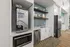 Modern kitchen area with a sleek beverage machine, microwave, and stainless steel appliances, enhanced by stylish tile backsplash and warm wood flooring.