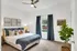 Model bedroom with modern decor, featuring a plush bed, elegant artwork, and a leafy indoor plant by a sunlit window.