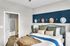 Chic bedroom featuring a plush bed with layered pillows, stylish hat decor on a modern blue accent wall, and an en suite bathroom with elegant wooden flooring.