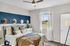 Charming bedroom with stylish decor, featuring an elegant bed with plush pillows, a chic hat display on a navy accent wall, and a large window with natural sunlight.