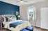 Inviting bedroom with elegant decor featuring a plush bed, stylish blue accent wall, and ample natural light through a large window.