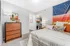 Inviting bedroom with cozy bed, vibrant wall art, and stylish wooden dresser, offering a glimpse into an elegant apartment interior.