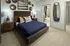 Contemporary bedroom featuring a plush bed with vibrant pillows, a stylish wall mirror, and elegant side tables with ambient lighting. Adjoining modern bathroom offers luxurious amenities, perfect for a cozy retreat.