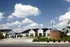 Charming residential community featuring modern homes with a welcoming entrance under a bright blue sky, lush landscaping, and stylish architecture.