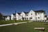 Charming apartment complex with modern white buildings, lush green lawns, and a relaxing outdoor seating area under string lights.