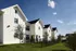 Charming row of modern townhouses with classic gabled roofs, surrounded by lush green lawns and clear blue skies.