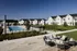 Charming community features modern white townhouses with a sparkling pool, lush green spaces, and cozy outdoor seating area.