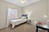 Bright bedroom with a cozy single bed, elegant side table lamp, and modern work desk, ideal for serene relaxation and productivity.