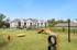 Charming apartment complex with modern architecture, adjacent to a vibrant dog park with agility equipment and greenery.
