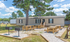 Charming manufactured home with modern exterior, nestled among lush greenery, featuring picnic tables and BBQ grills for outdoor entertainment.