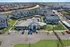 Aerial view of stylish apartment complex with modern gray buildings, landscaped paths, a sparkling central pool, and ample parking, set in a vibrant residential neighborhood.