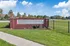 Inviting entrance to Fairways at Lincoln Apartments, featuring a charming red brick sign surrounded by lush greenery and a serene community vibe.