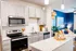 Modern kitchen with sleek white cabinets, stainless steel appliances, and granite countertops, opening to a vibrant living area with colorful decor.