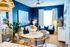 Vibrant modern living room with blue accent wall, stylish seating, and a chic dining area featuring woven chairs and a marble table.