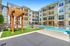 Vibrant apartment complex showcasing a sparkling pool, lush green lawn, and relaxing seating areas under elegant wooden pergolas.