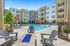 Elegant apartment complex with a pristine swimming pool, sun loungers, and modern outdoor seating in a lush courtyard setting.