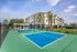 Elegant apartment complex with modern tennis court, surrounded by lush greenery and palm trees, offering active lifestyle amenities.