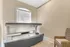 Bright room featuring a modern tanning bed with natural light streaming through an arched window and a stylish woven chair.