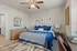 Elegant bedroom with plush blue bedding, stylish decor, and ample natural light, featuring a chic ceiling fan and cozy wooden furniture.