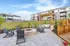 Charming landscaped courtyard with modern fire pit, cozy seating area under a stylish pergola, surrounded by lush greenery and contemporary apartments.