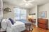 Inviting bedroom with natural light, featuring a cozy bed, modern lighting, sleek workspace, and stylish wooden flooring.