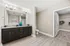 Elegant bathroom featuring a double-sink vanity with granite countertops, contemporary lighting fixtures, luxurious flooring, and an adjacent spacious walk-in closet.