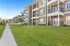 Charming modern apartments with private balconies, nestled in lush green landscaping under a bright blue sky.