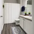 Elegant bathroom featuring modern vanity with polished countertop, chic white cabinetry, stylish shower curtain, and warm wood floors enhanced by a decorative rug.