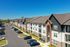 Modern apartment complex with three-story buildings, spacious balconies, and ample parking under a clear blue sky.