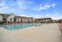 Inviting outdoor swimming pool area with cozy seating under a gazebo, surrounded by modern apartment buildings and a clear blue sky.