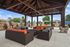 Elegant outdoor pavilion with cozy seating area featuring stylish wicker sofas and vibrant cushions under a wooden-beamed roof.